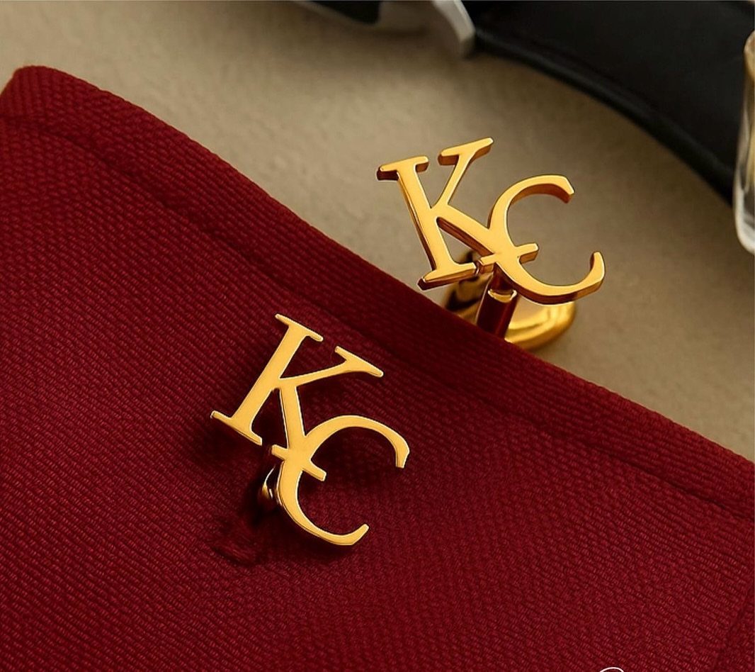 Gold cufflinks with intertwined KC initials resting on a red fabric background.