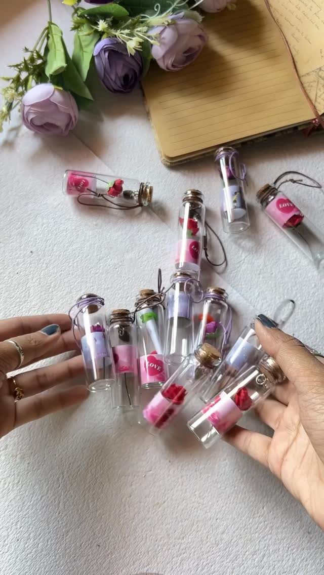 Small glass vials with rolled notes and petals held by two hands.