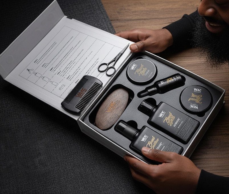 Beard grooming kit in a black box with scissors, comb, and oils.
