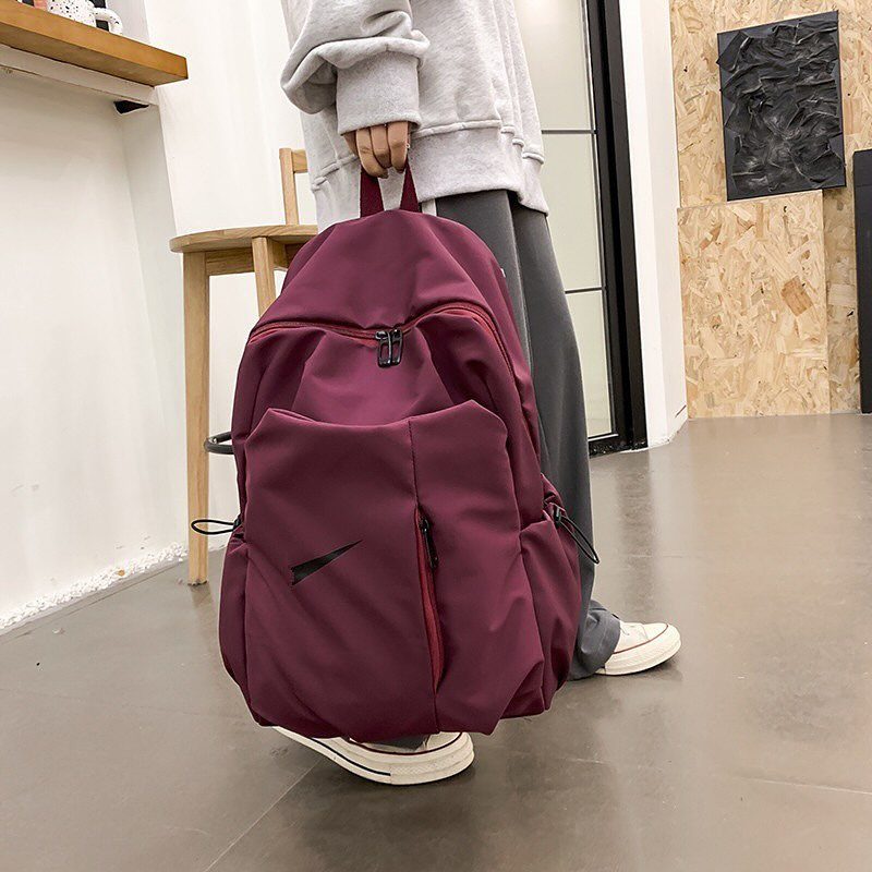 Maroon nylon backpack held by a person in grey casual clothing indoors.