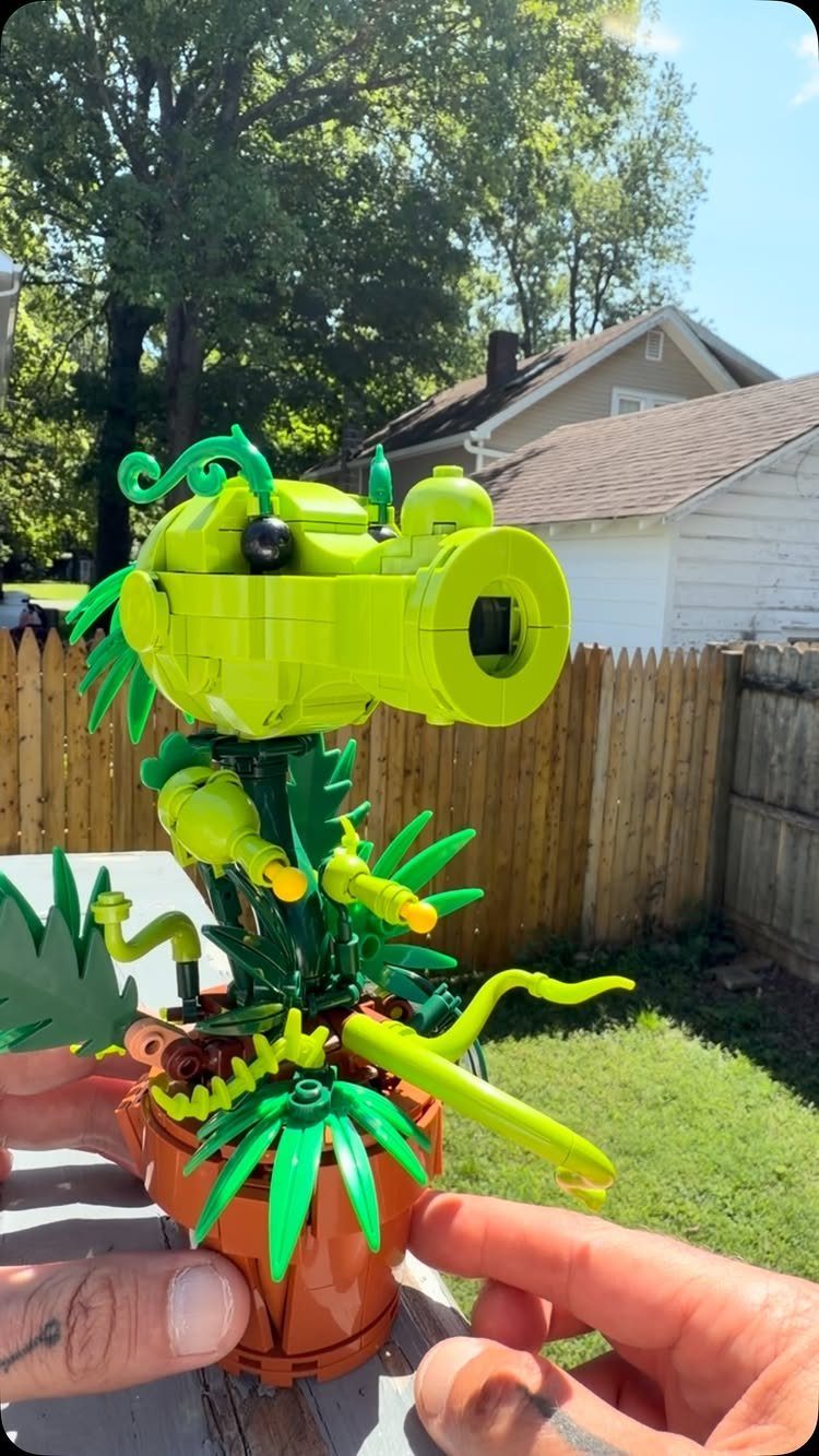 Green Lego carnivorous plant in a brown pot held by two hands outdoors.
