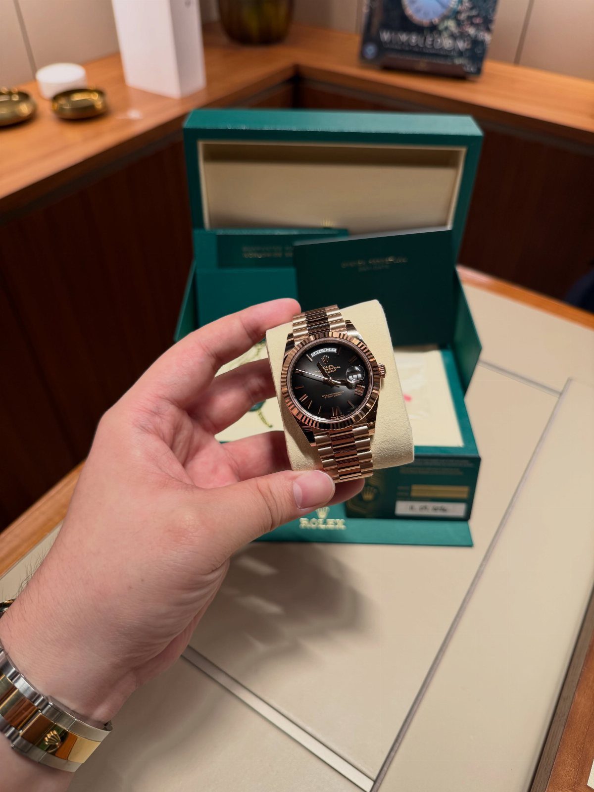 Gold luxury wristwatch with black face held over a green branded watch box.