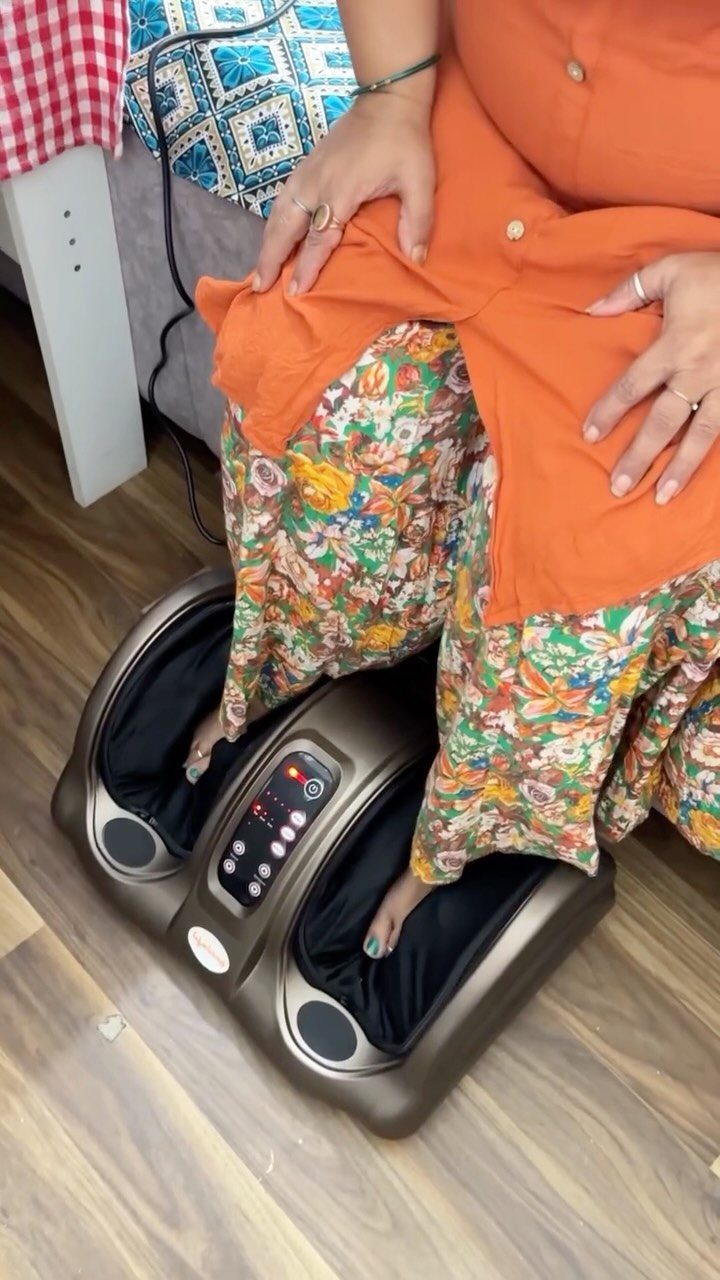 Person using a bronze electric foot massager while wearing orange and floral clothing.