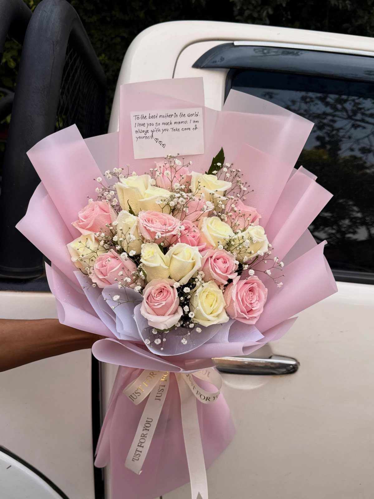 Bouquet of pink and white roses wrapped in purple paper with a note.