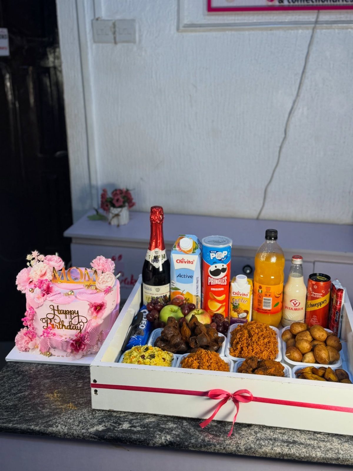 Pink birthday cake and a white gift crate filled with champagne and snacks.