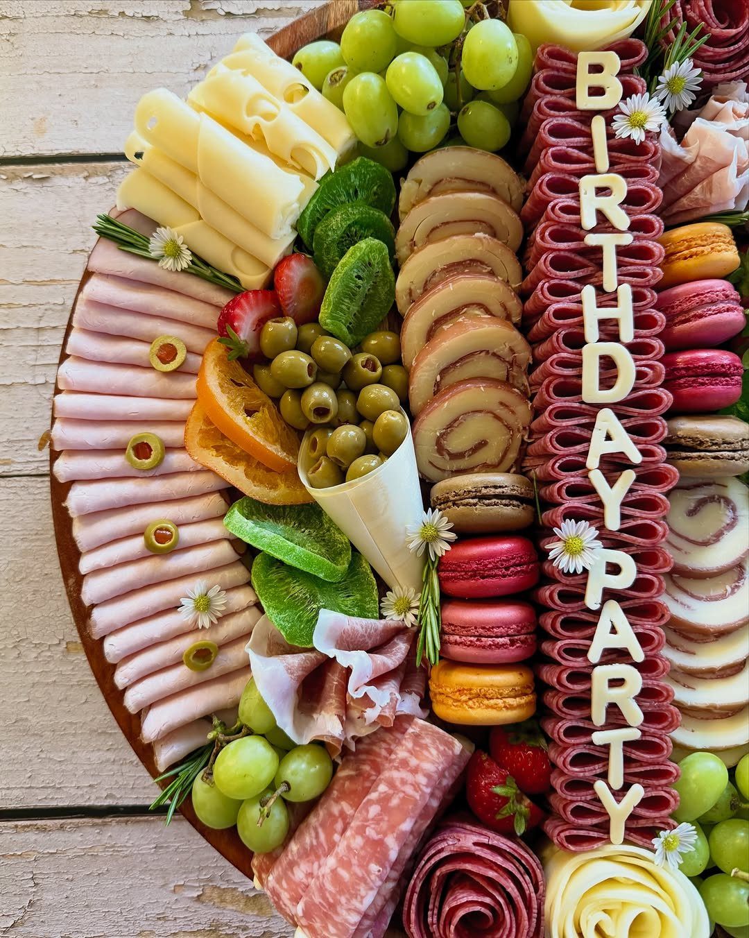 Wooden charcuterie board with meats, cheeses, and fruits spelling BIRTHDAY PARTY in salami.