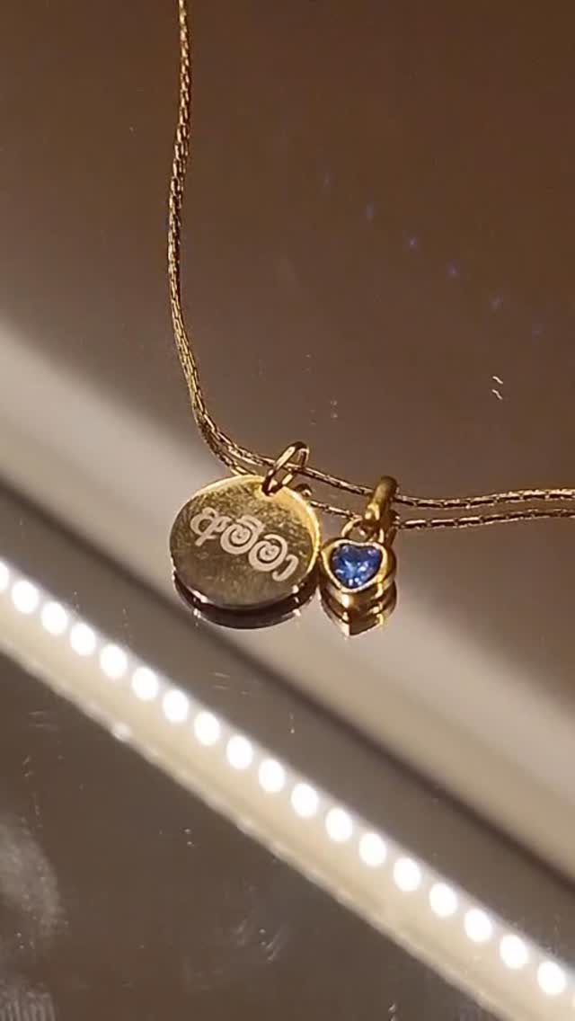 Gold necklace with an engraved circular charm and a blue birthstone heart pendant.