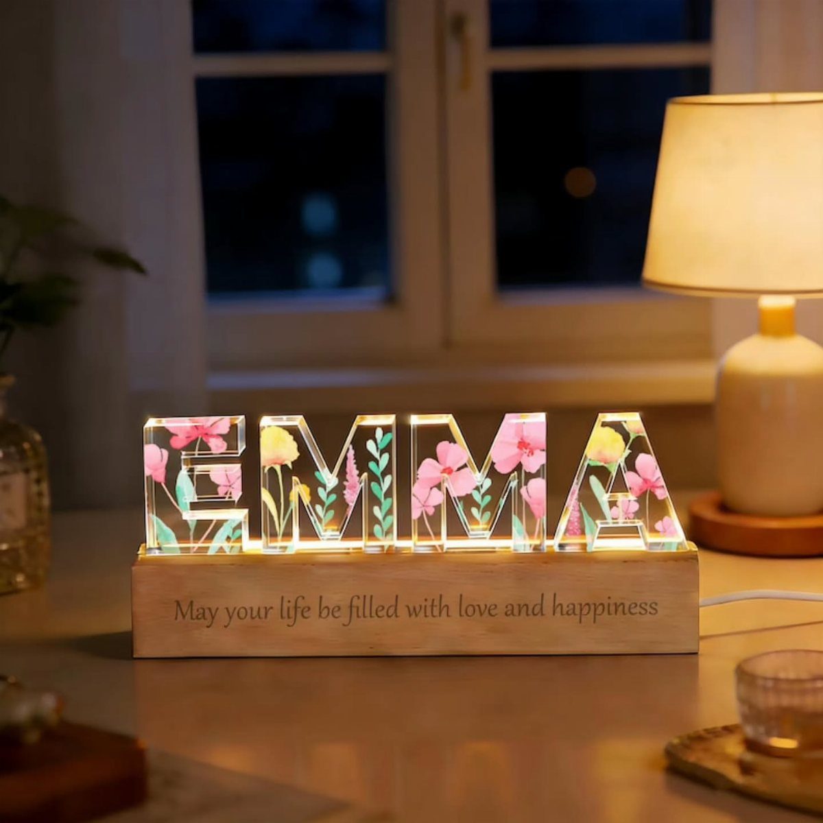 Illuminated acrylic name lamp spelling EMMA with floral designs on a wooden base.