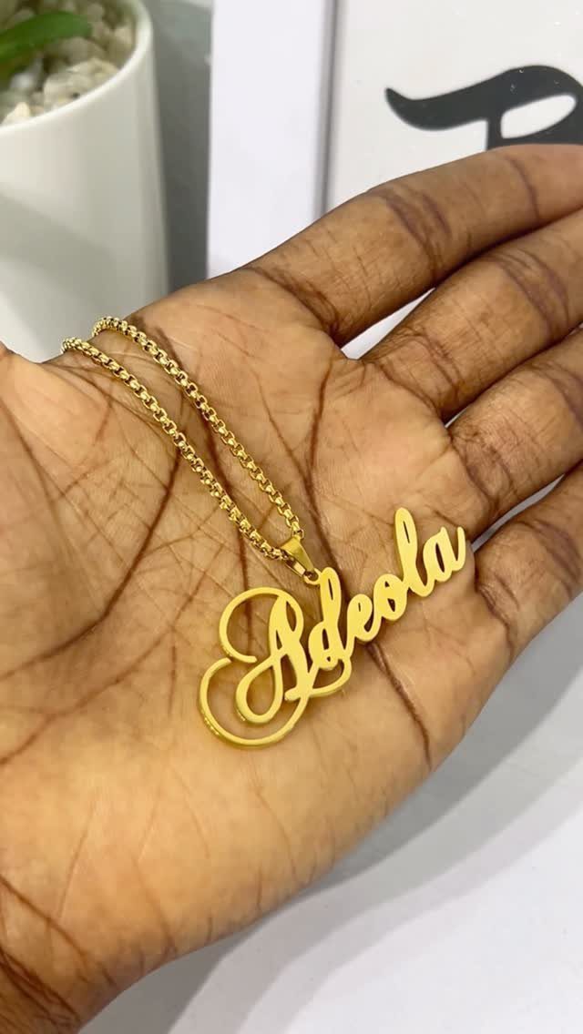 Gold nameplate necklace spelling Adeola resting on a person's open palm.