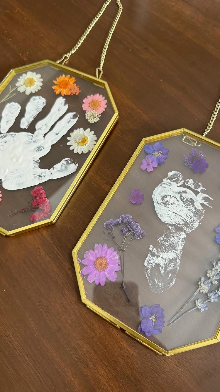 Two hexagonal gold glass pendants with white handprints and colorful pressed dried flowers.