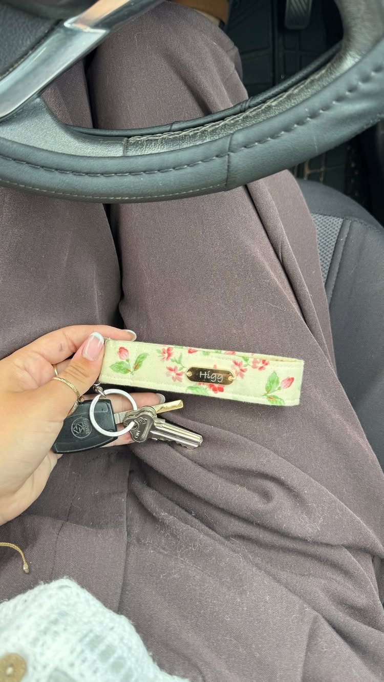 Floral fabric wristlet keychain with a personalized nameplate held with car keys.