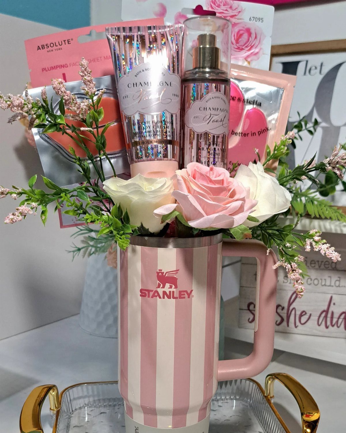 Pink striped Stanley tumbler filled with roses, lotion, and perfume on a tray.