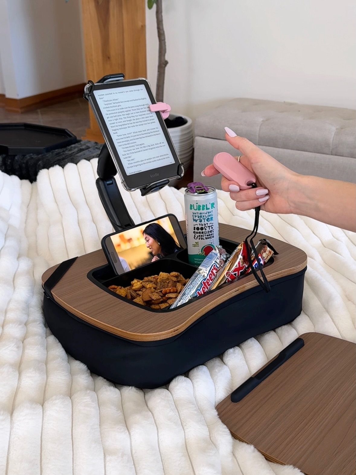 Bed tray with e-reader, smartphone, and snacks on a white fluffy blanket