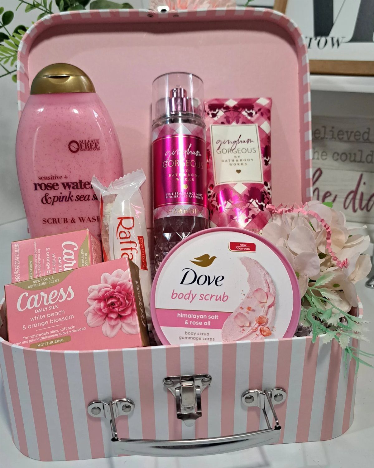 Beauty products and pink flowers arranged inside a pink striped suitcase gift set.