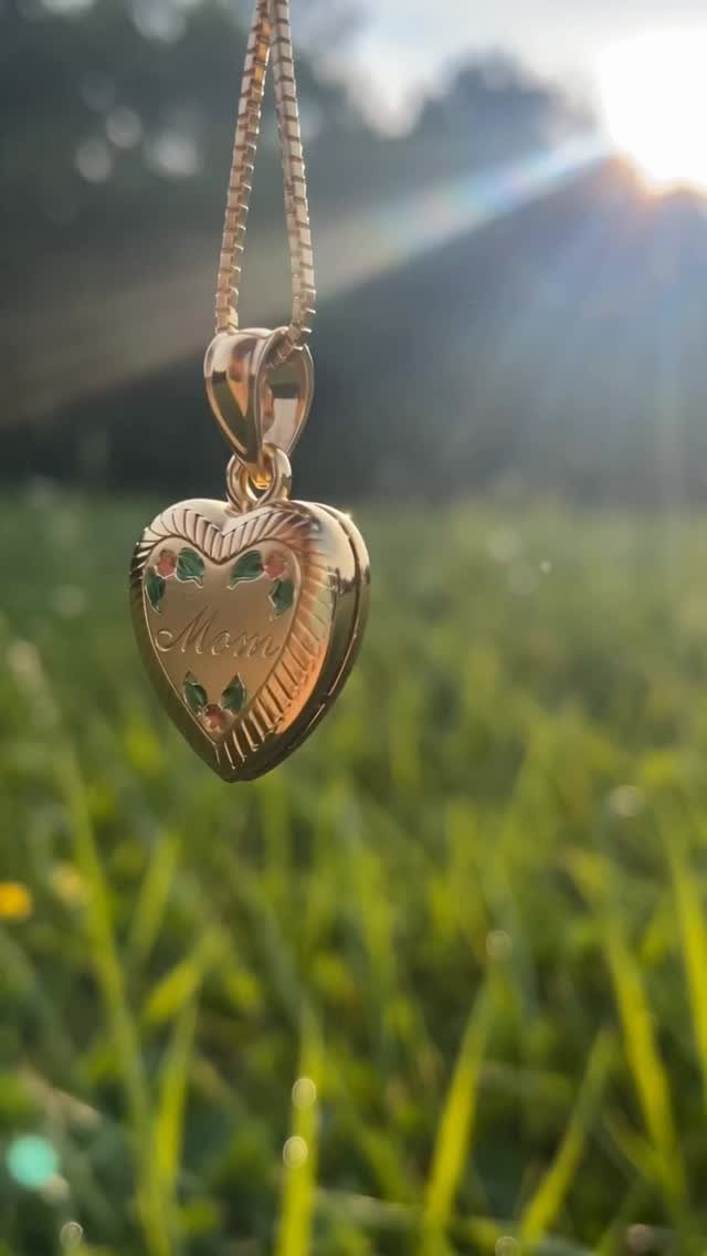 Gold heart-shaped locket necklace engraved with Mom hanging over a sunny green lawn
