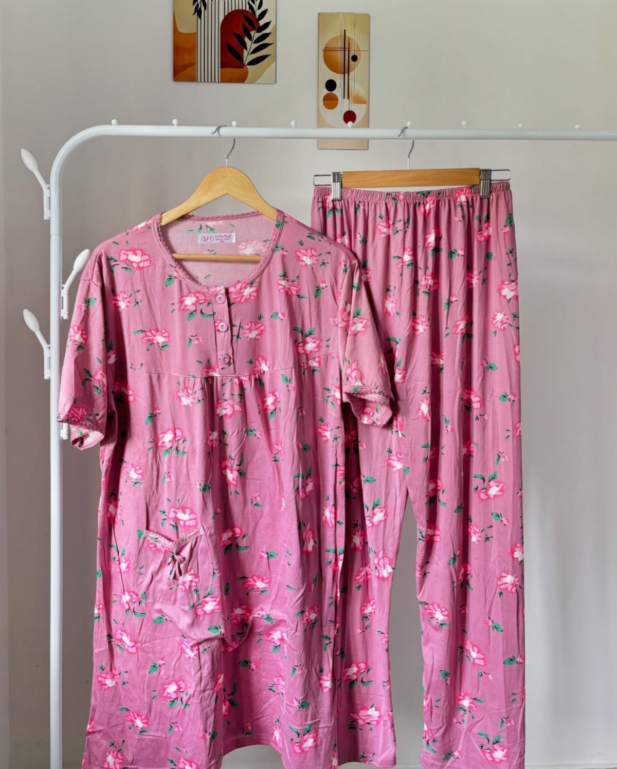 Pink floral pajama set hanging on a white clothing rack against a wall