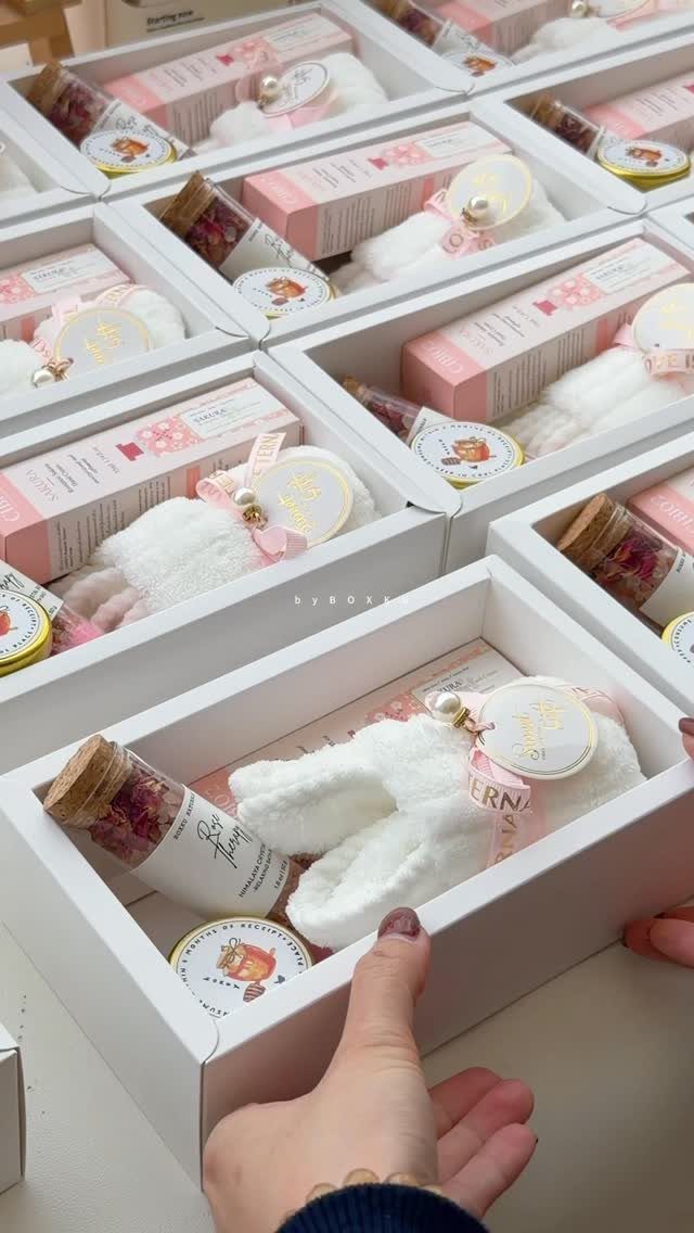 White gift boxes filled with pink skincare products and fluffy white slippers.