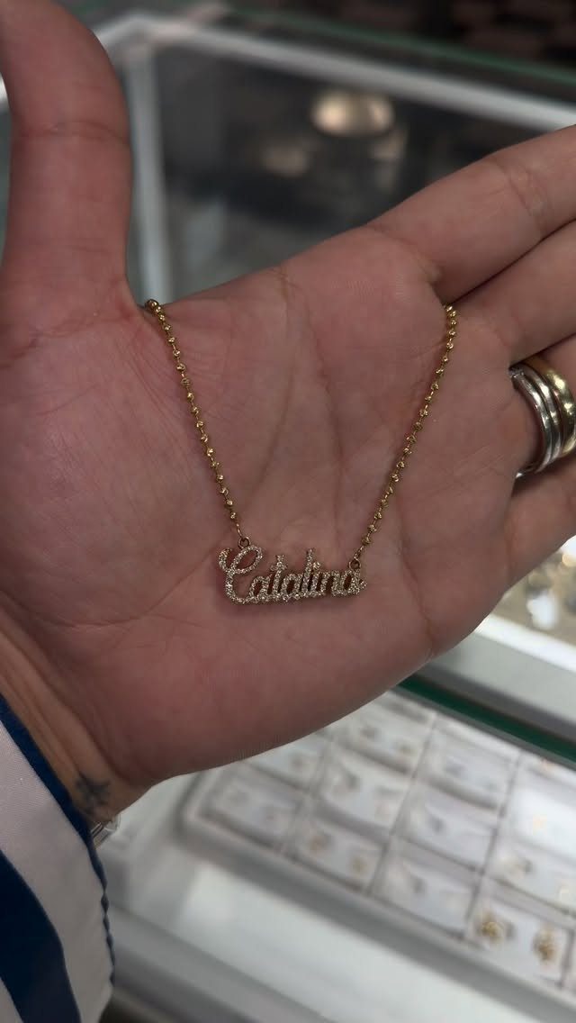 Gold nameplate necklace reading Catalina held in a person's open palm.