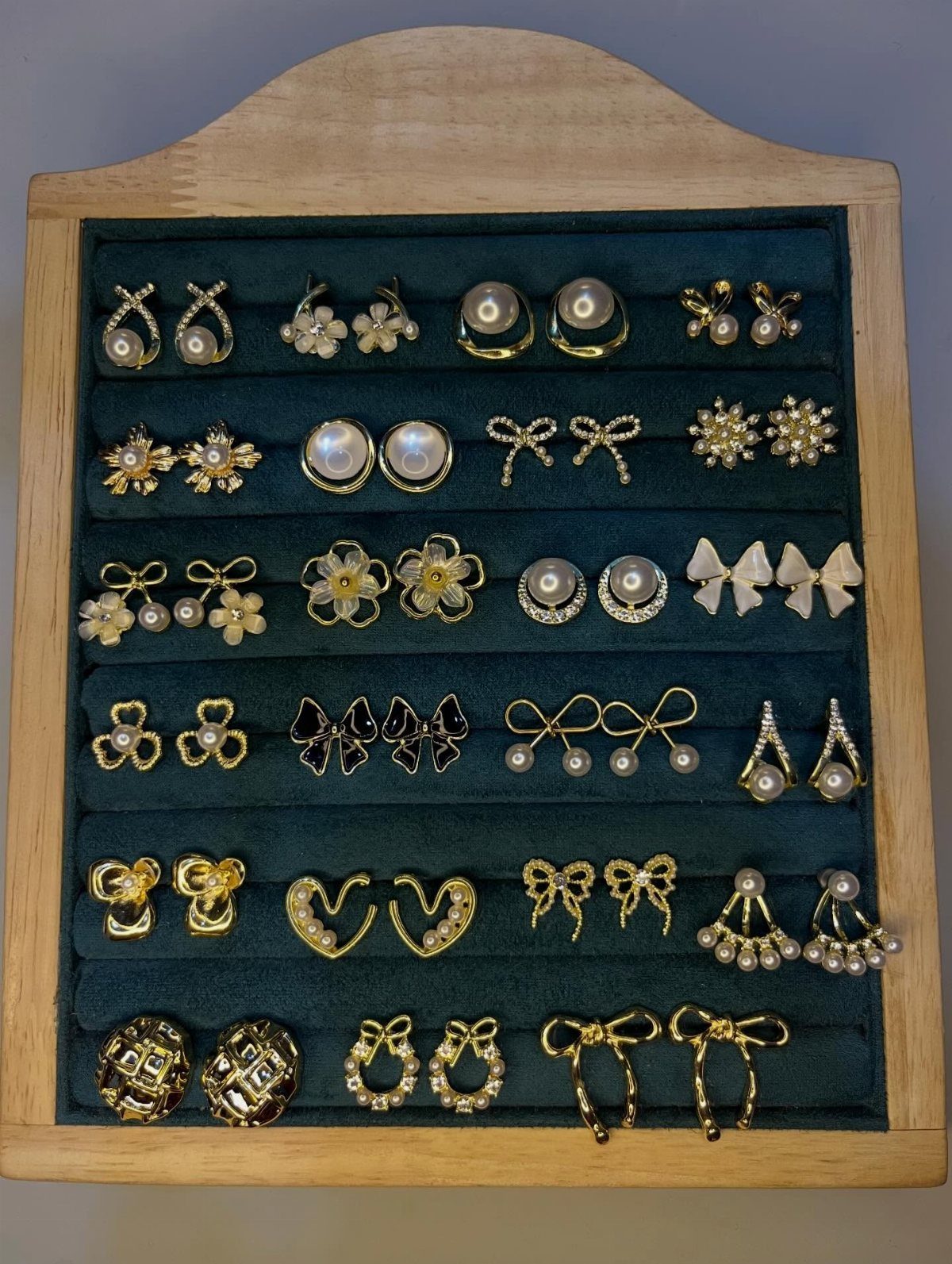 Gold and pearl earrings displayed in a wooden case with green velvet lining.