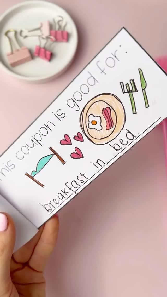Hand holding a handmade breakfast in bed coupon with colorful drawings on white paper.