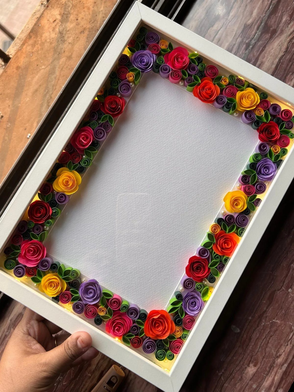 White frame with a border of colorful rolled paper roses and green leaves.