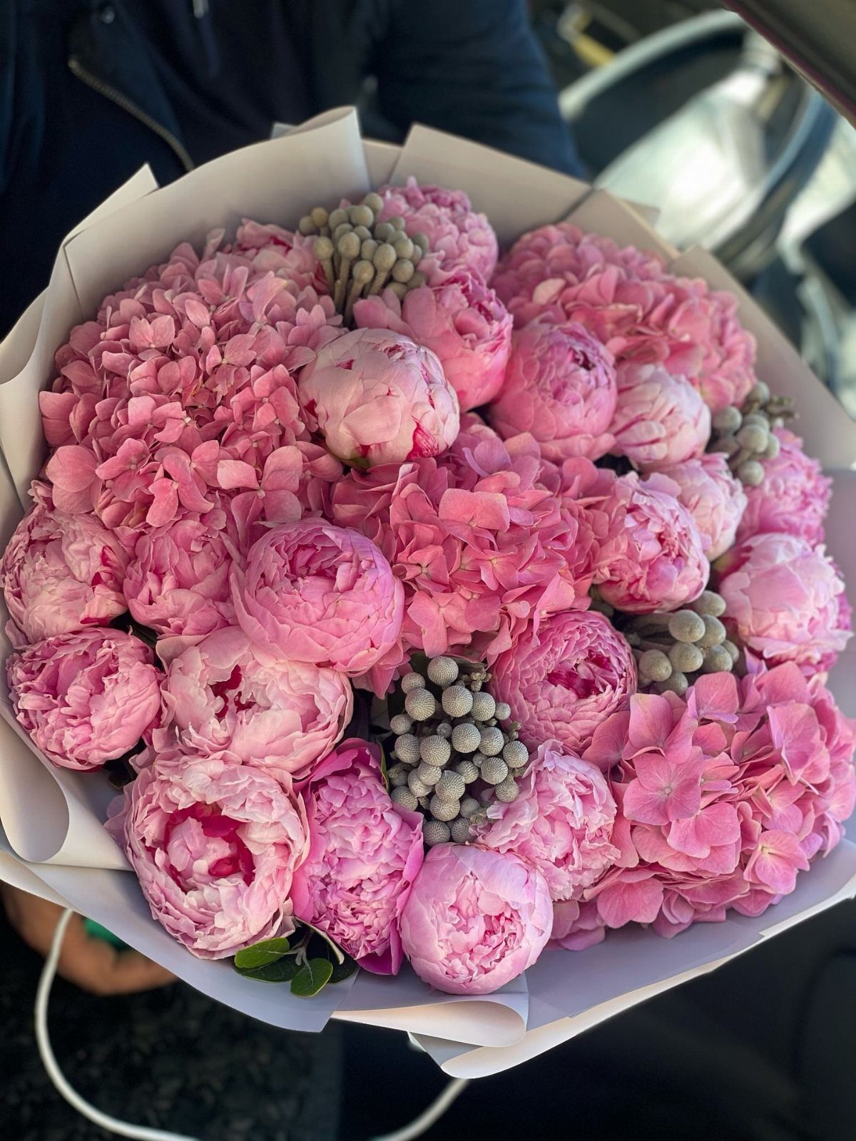 Pink peony and hydrangea bouquet wrapped in white paper with small grey berries