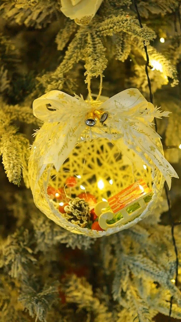 Woven cream ornament with a white bow and pinecone on a frosted tree