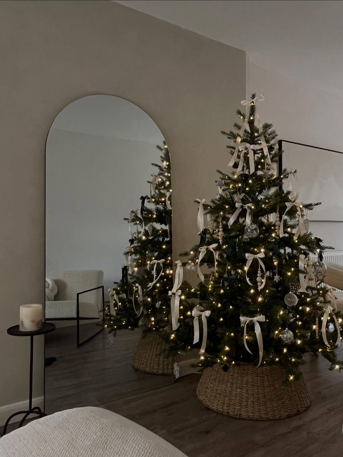 Decorated Christmas tree with white ribbons in a wicker basket reflected in arched mirror