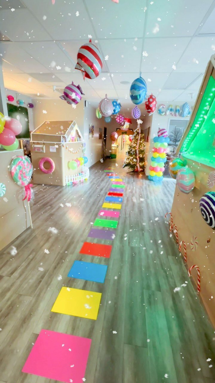 Colorful office hallway decorations featuring a cardboard house, balloons, and a Christmas tree.