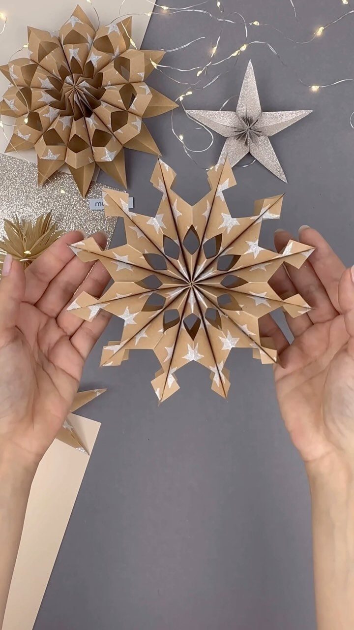 Hands holding a 3D folded brown and white paper snowflake decoration.