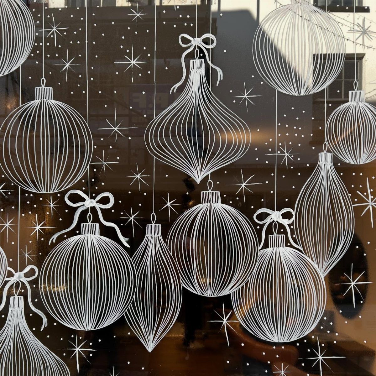 White painted Christmas ornaments and stars on a glass window pane.