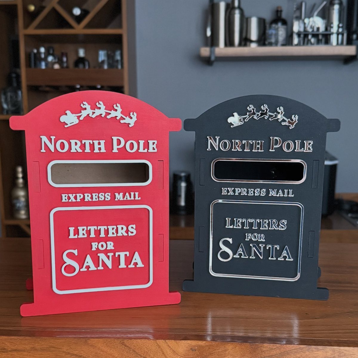 Red and black North Pole mailboxes for letters to Santa on a table.