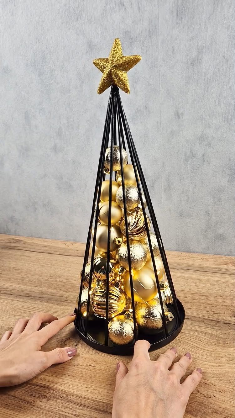 Cone-shaped black wire Christmas tree filled with gold ornaments on a wooden table