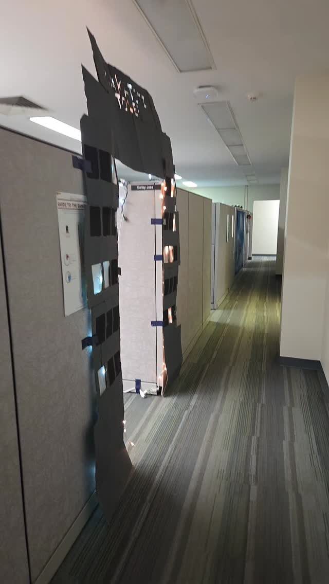 Black cardboard city skyline cutout with lights decorating an office cubicle entrance.