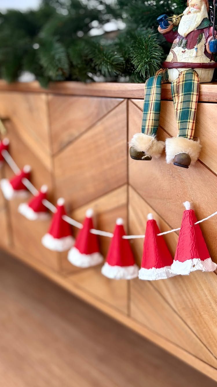 Santa hat garland and Santa figurine decorating a wooden cabinet with pine branches
