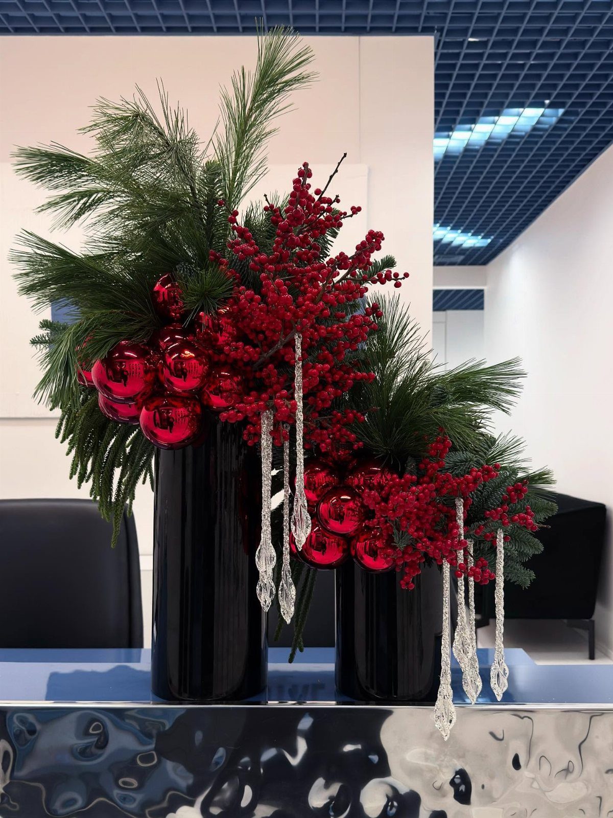 Holiday floral arrangement with red ornaments and pine branches in black vases.