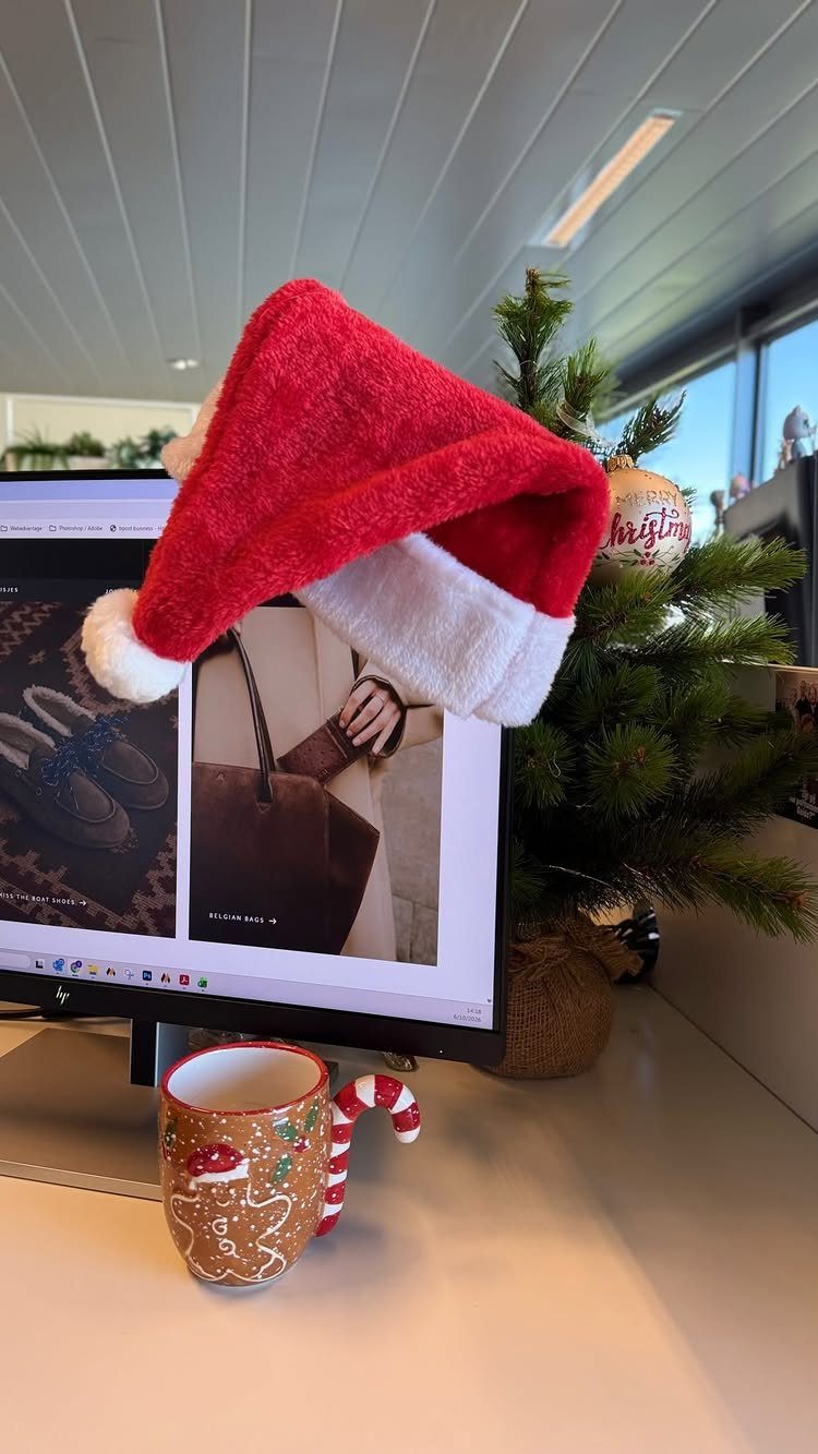 Santa hat on a computer monitor with a small Christmas tree and festive mug.