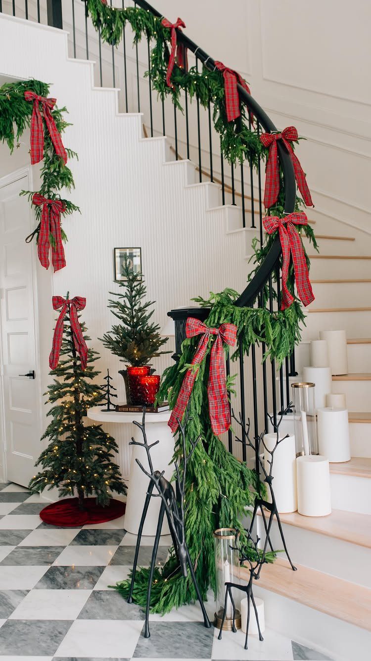 Staircase decorated with green garlands and red plaid bows in a home entryway