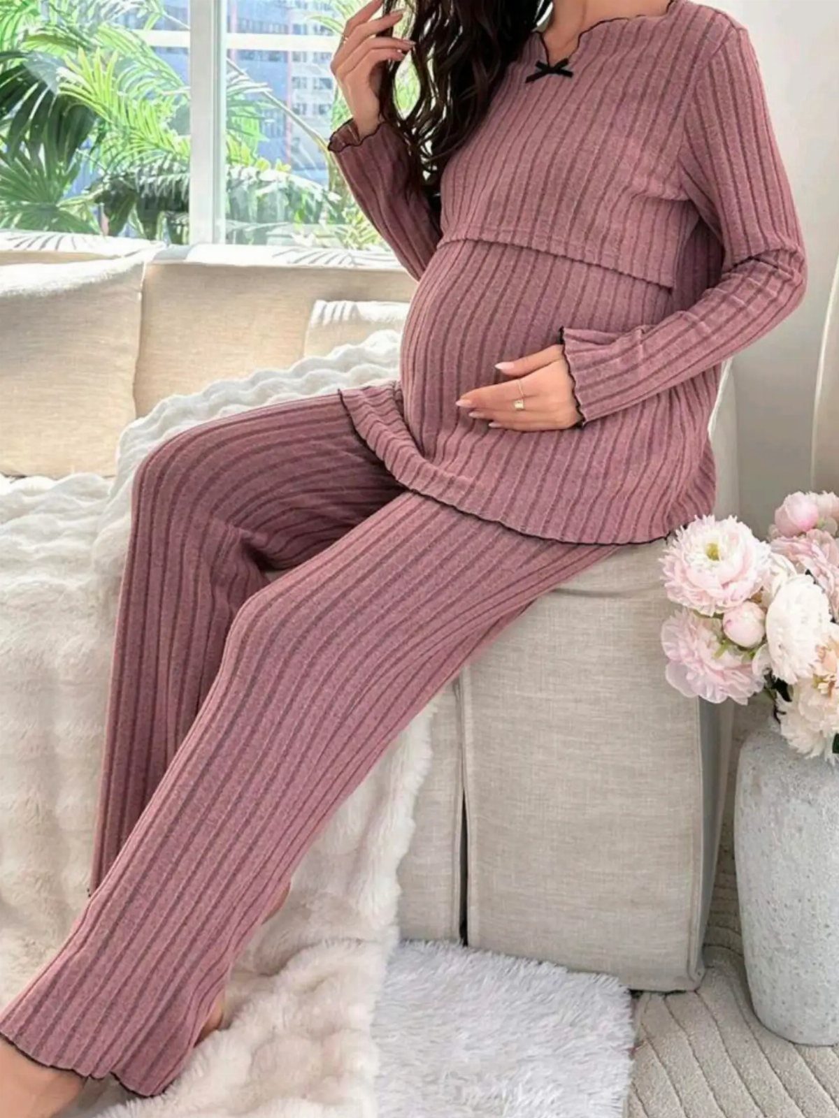 Pregnant woman wearing a mauve ribbed knit loungewear set sitting on a white sofa