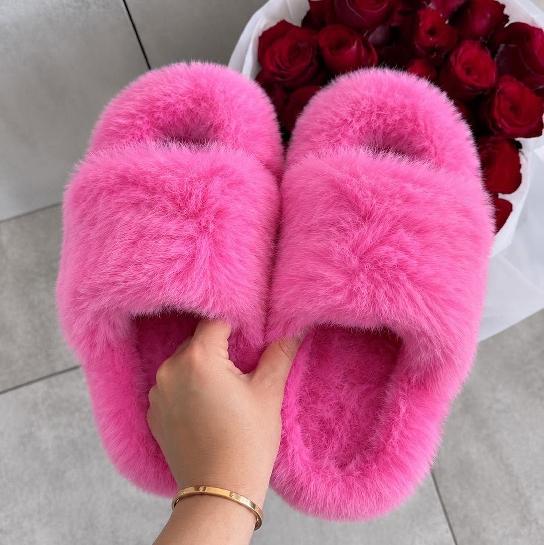 Bright pink faux-fur slippers held by a hand with red roses in background