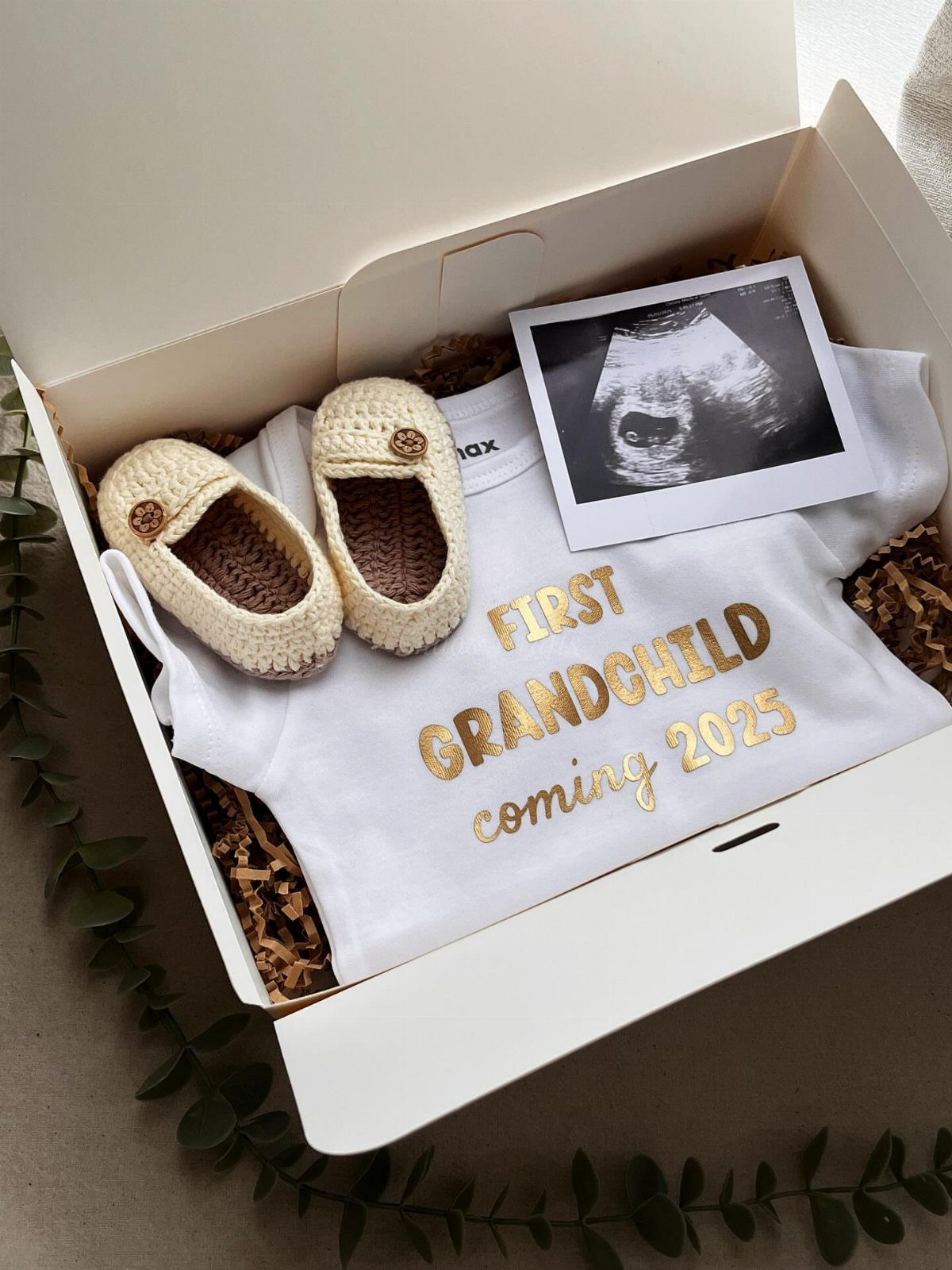 Pregnancy gift box with baby onesie, knitted shoes, and an ultrasound photo.