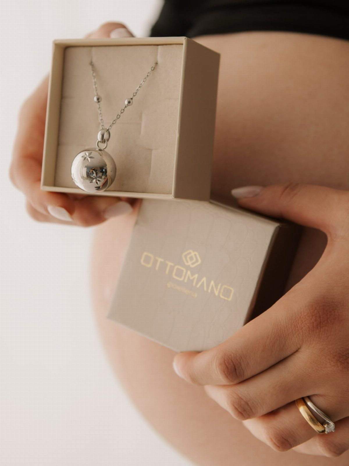 Silver harmony ball necklace in a beige box held against a pregnant belly
