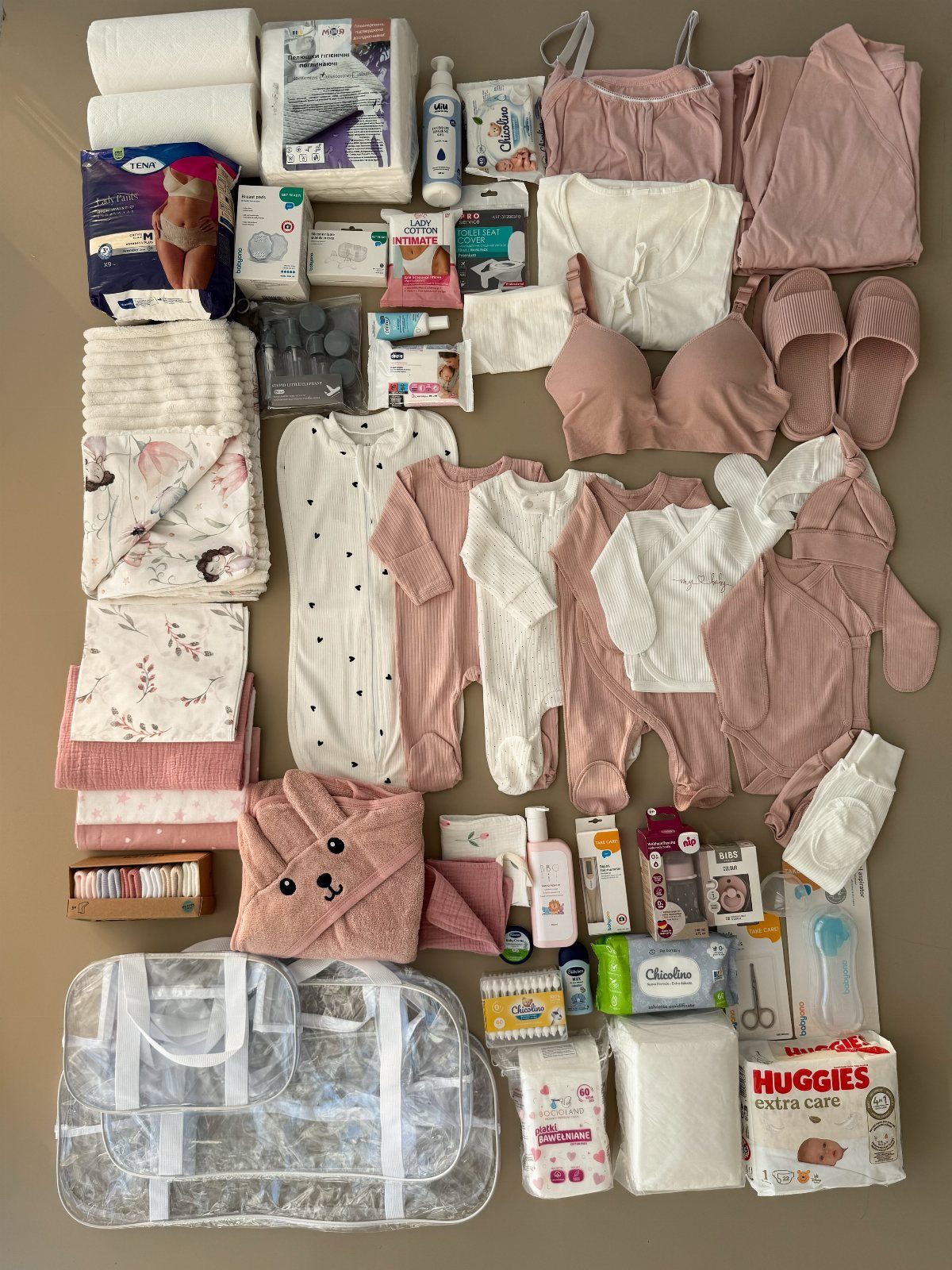 Maternity and baby essentials including pink clothing, diapers, and toiletries arranged on a surface.