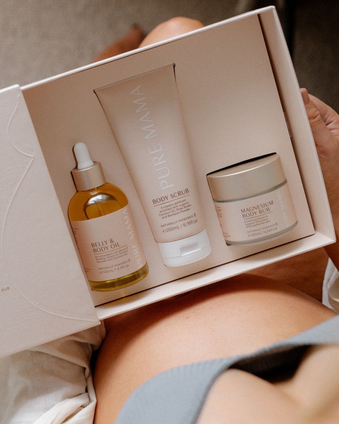 Pregnancy skincare gift set in a white box held over a pregnant belly