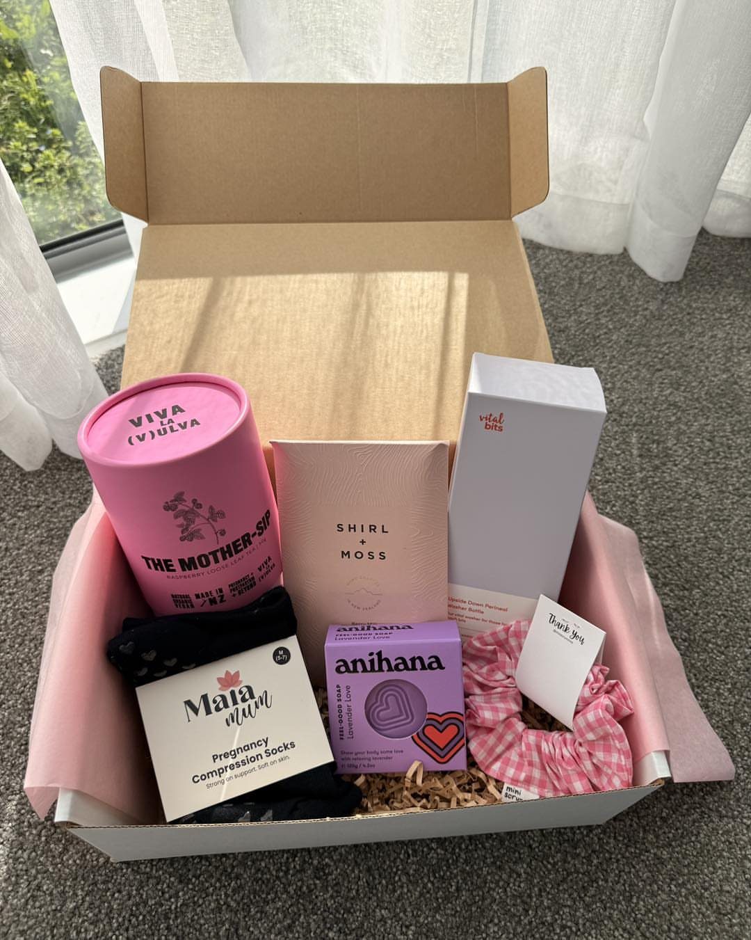 Gift box containing pregnancy compression socks, a pink tumbler, and various skincare products.