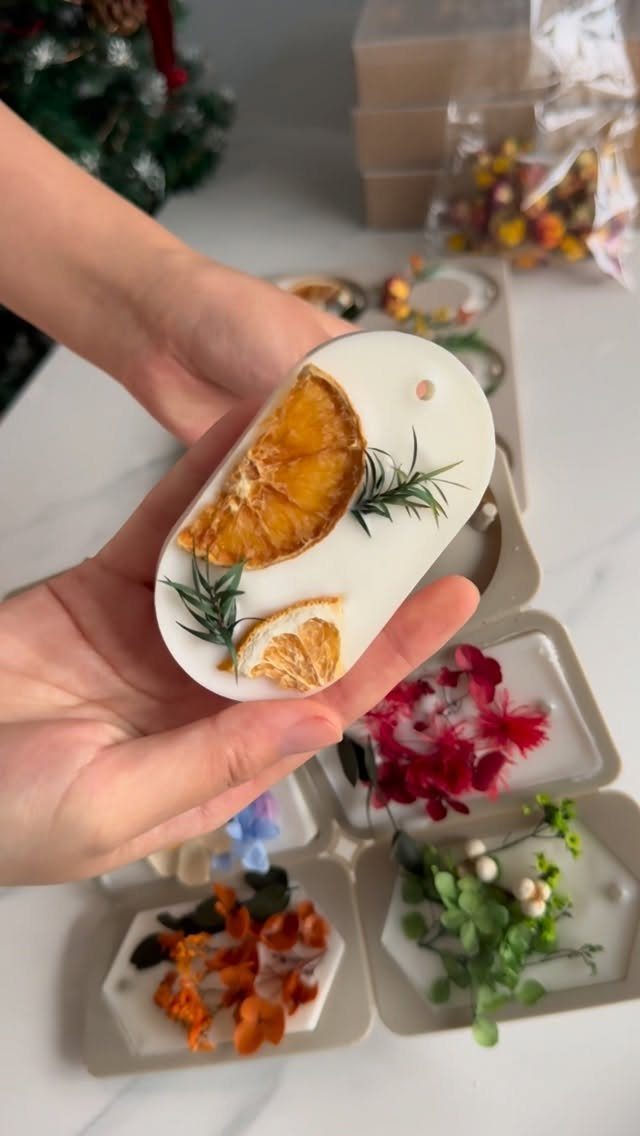 White botanical wax sachet with dried orange and rosemary held in hands.