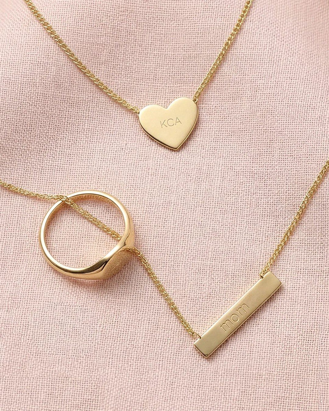 Gold engraved necklaces with heart and bar pendants on pink textured fabric