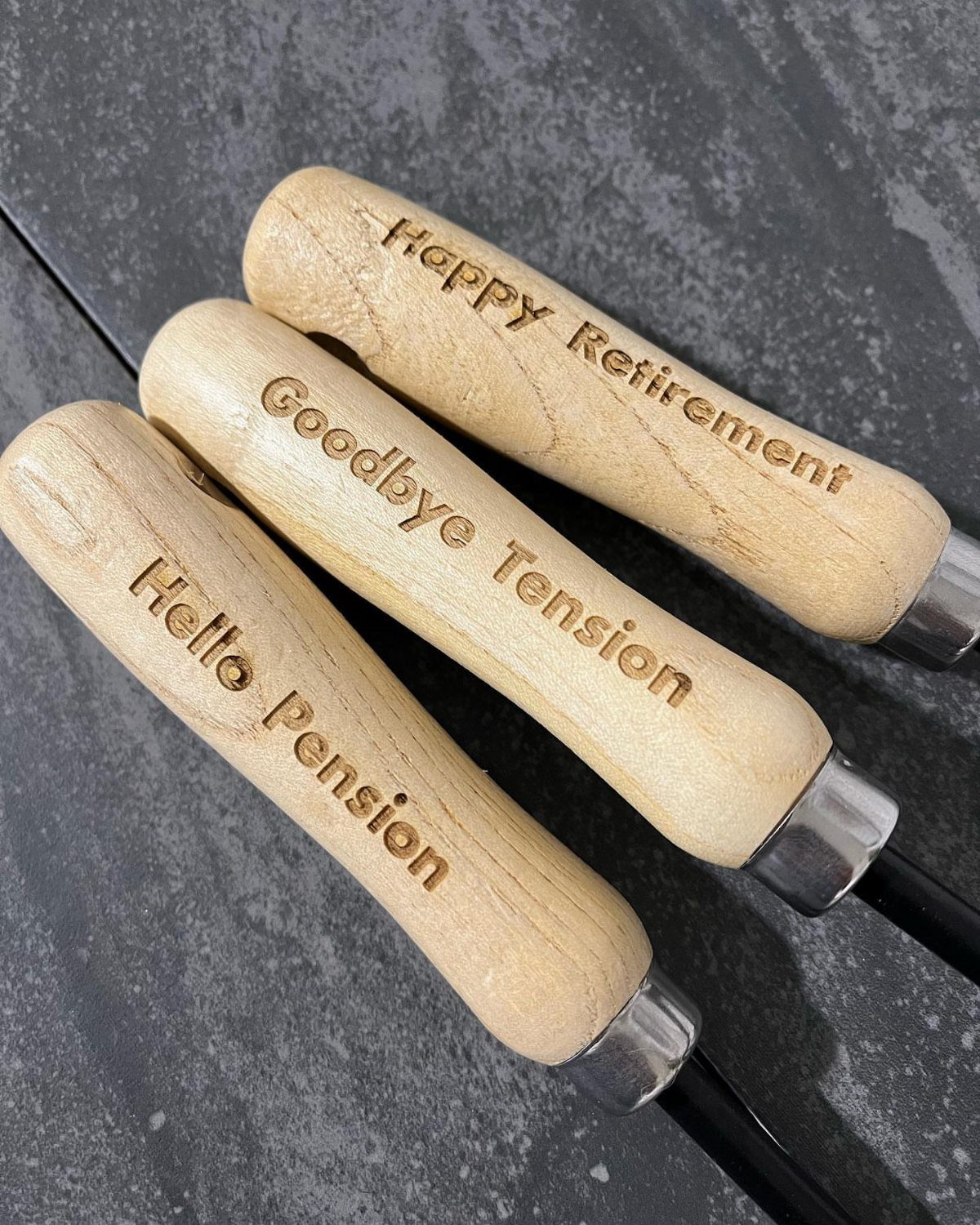 Engraved wooden handles of gardening tools with retirement messages on dark grey background