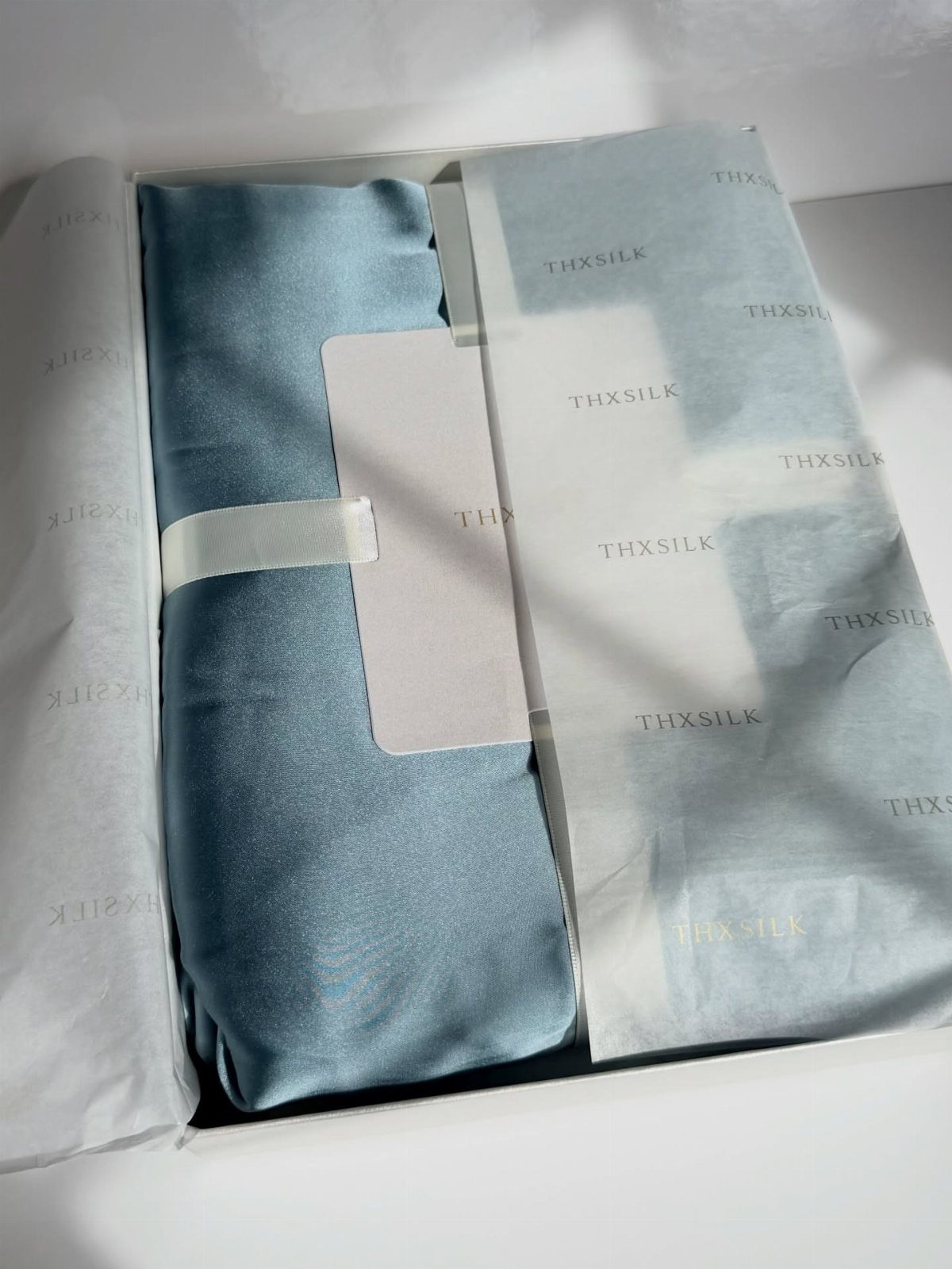 Light blue silk pillowcase folded in a white gift box with branded tissue paper