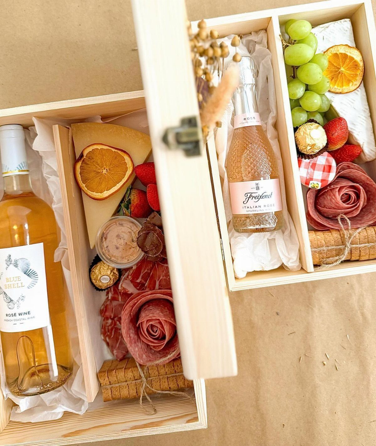Two wooden gift boxes filled with rosé wine, cheese, grapes, and cured meats.